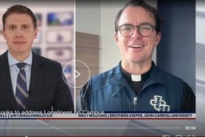 A man in a suit and tie is on the left side of the screen, while a man wearing glasses and a clerical collar is on the right.