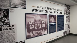 A wall display titled David Rastoka ’90 Athletics Hall of Fame shows a large photo of a football player in jersey number.