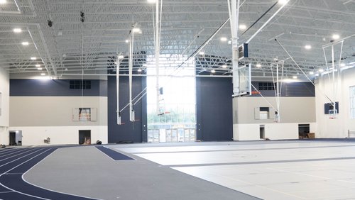 A large indoor sports facility with a blue running track curving around a multi-use court under bright ceiling lights.