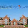 A large brick university building with many windows stands behind a sign reading John Carroll University under a clear blue.