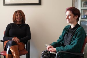 Two Women Sit Chairs Facing Each Other One